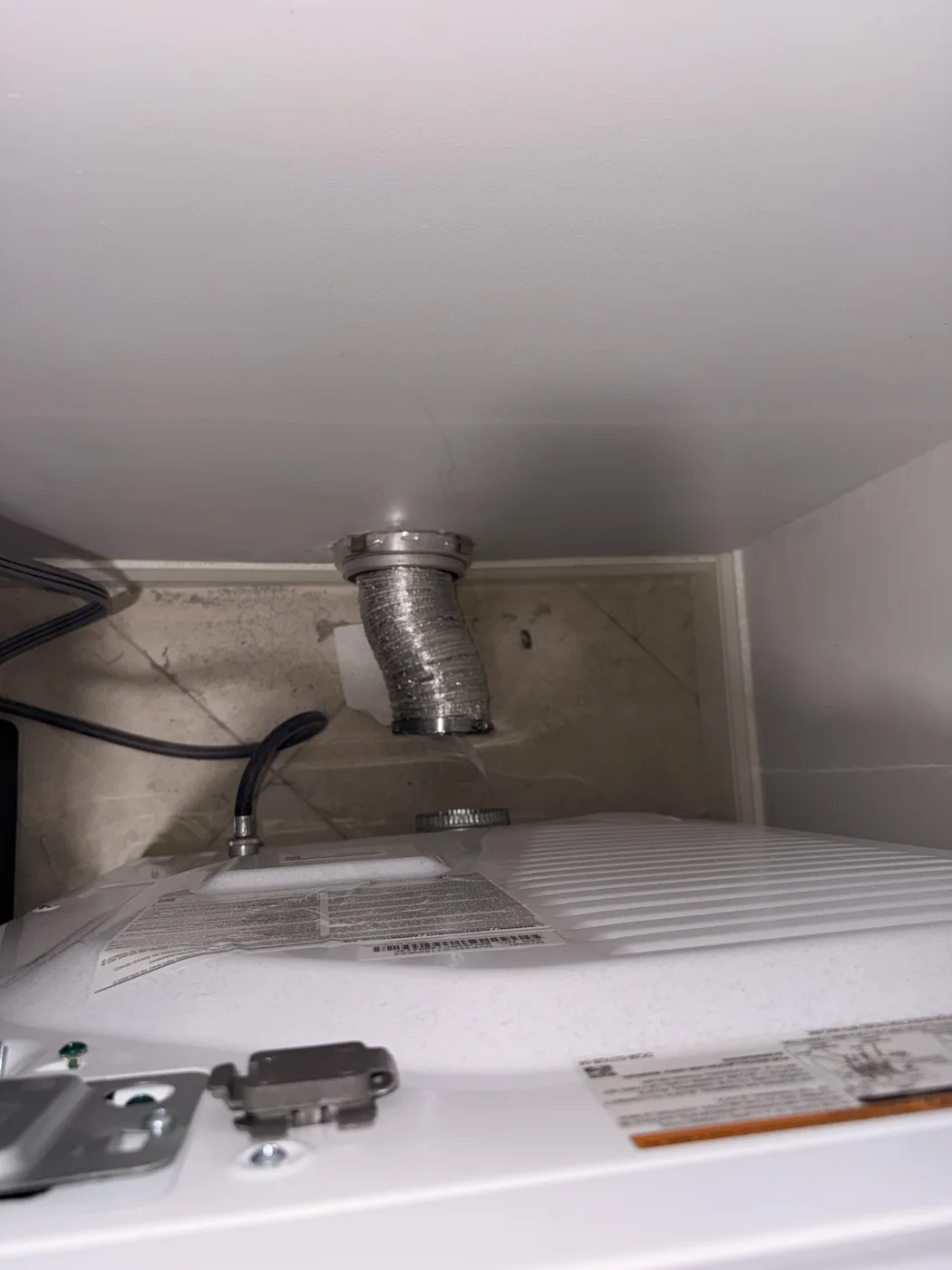 Post-service view of the short dryer connector behind a stacked appliance